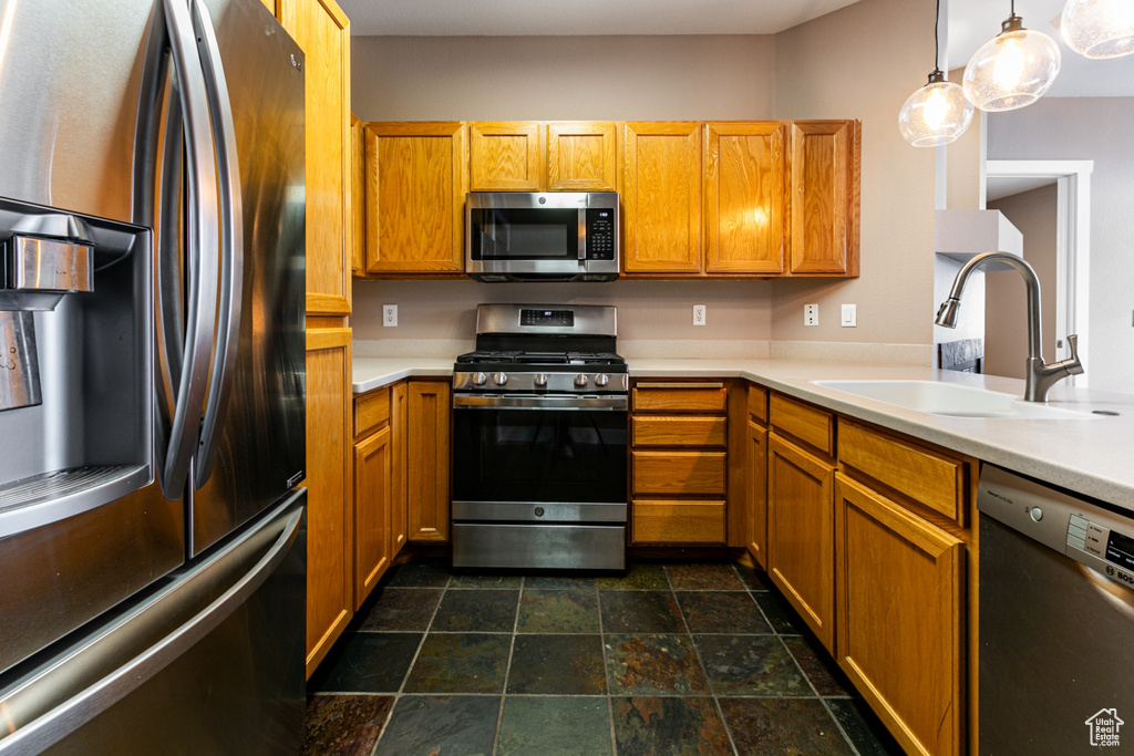 Kitchen featuring stainless steel appliances, light countertops, dark stone finish floors, and brown cabinetry