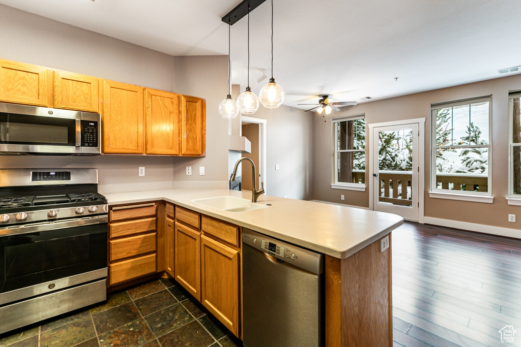 Kitchen with appliances with stainless steel finishes, a peninsula, ceiling fan, light countertops, and hanging light fixtures