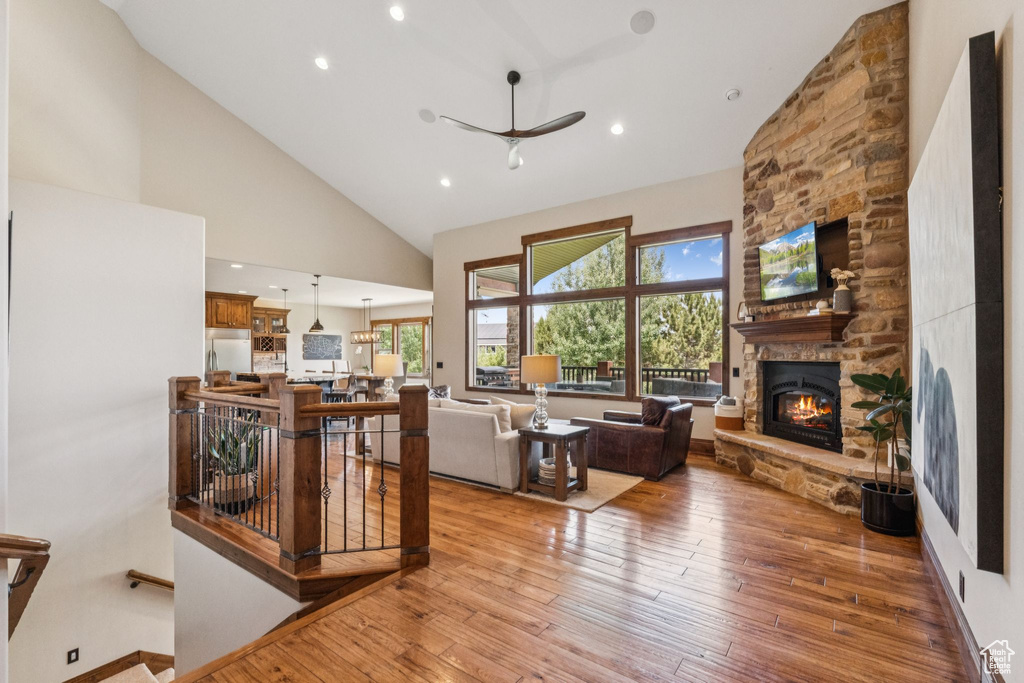 Living room with a stone fireplace, high vaulted ceiling, a ceiling fan, hardwood / wood-style flooring, and recessed lighting