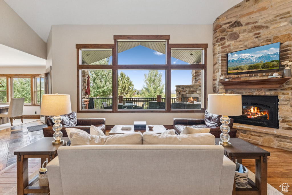 Living room with a stone fireplace, vaulted ceiling, and wood finished floors