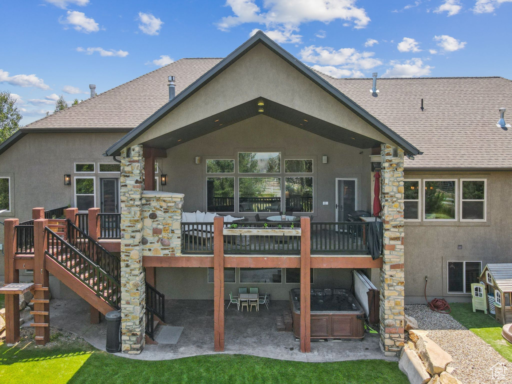 Back of property featuring stucco siding, a hot tub, and roof with shingles
