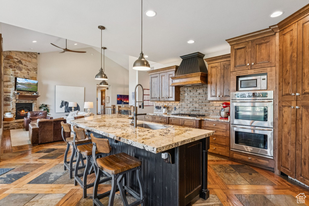 Kitchen with appliances with stainless steel finishes, premium range hood, open floor plan, decorative backsplash, and a fireplace