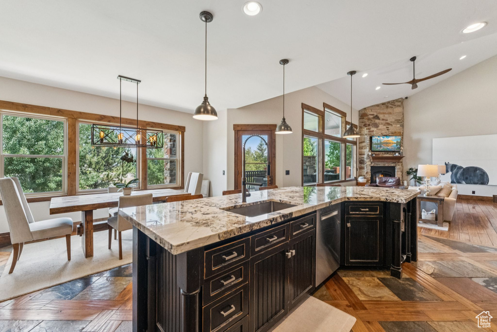 Kitchen with dark cabinetry, dishwasher, open floor plan, a large fireplace, and vaulted ceiling