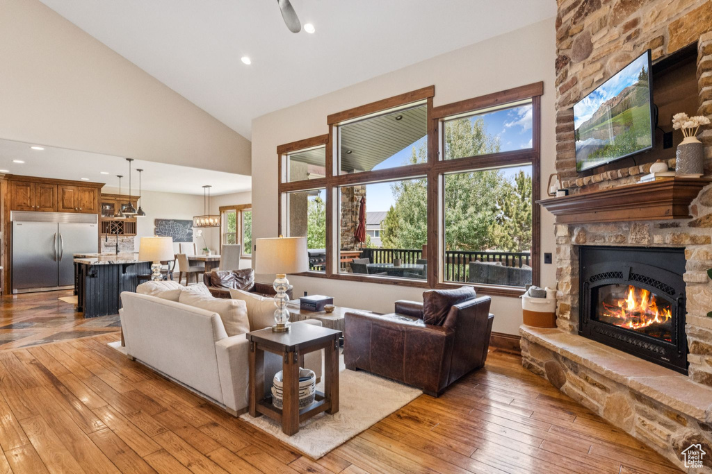 Living area featuring a stone fireplace, high vaulted ceiling, light wood-type flooring, and recessed lighting