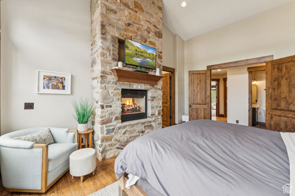 Bedroom featuring a fireplace, wood finished floors, high vaulted ceiling, and connected bathroom