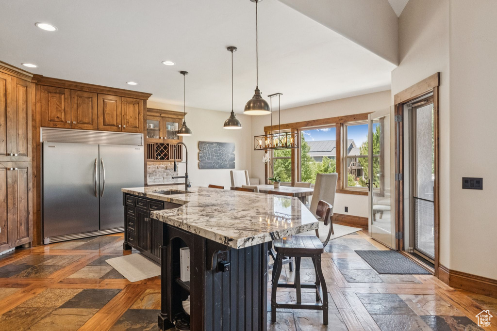 Kitchen featuring stainless steel built in fridge, brown cabinets, recessed lighting, a breakfast bar, and hanging light fixtures