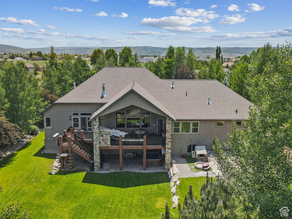 Back of house featuring a deck with mountain view, roof with shingles, a patio area, a yard, and stucco siding