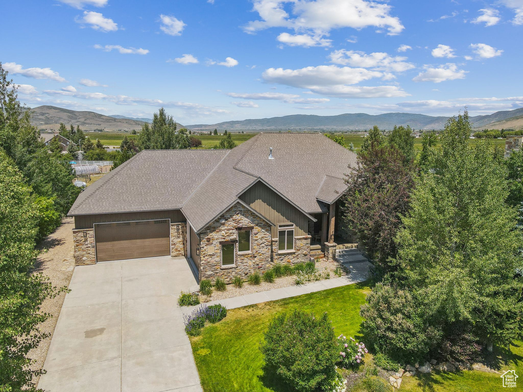 View of front of property with stone siding, roof with shingles, an attached garage, concrete driveway, and a mountain view