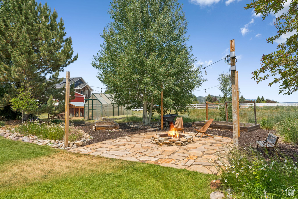 View of yard featuring a greenhouse, a fire pit, an outdoor structure, a patio, and a vegetable garden