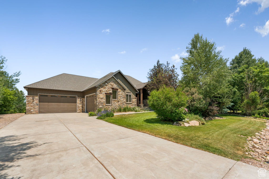 View of front of property with an attached garage, stone siding, concrete driveway, and a front lawn