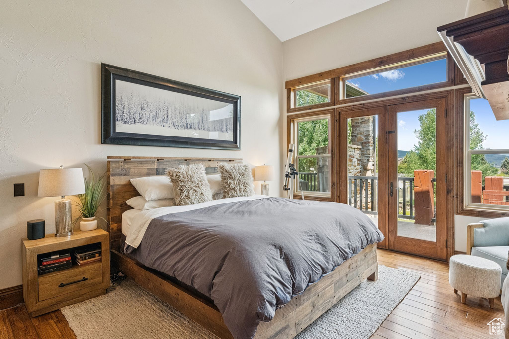 Bedroom with access to exterior, light wood finished floors, french doors, and lofted ceiling
