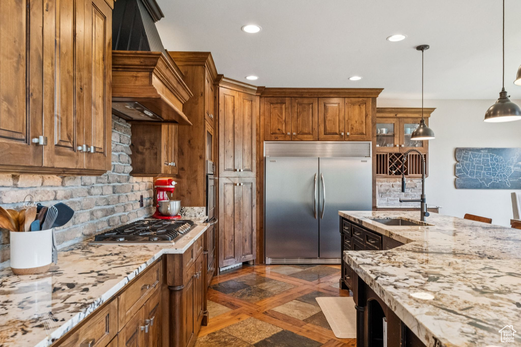Kitchen featuring appliances with stainless steel finishes, custom range hood, brown cabinetry, backsplash, and recessed lighting