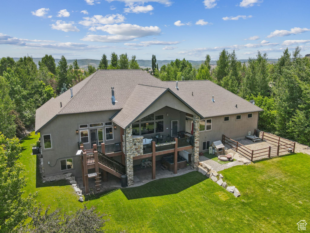 Rear view of property with a wooden deck, roof with shingles, a yard, stairs, and stone siding
