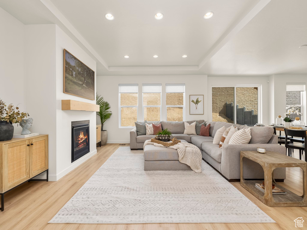 Living room with a tray ceiling, a glass covered fireplace, light wood-type flooring, and recessed lighting