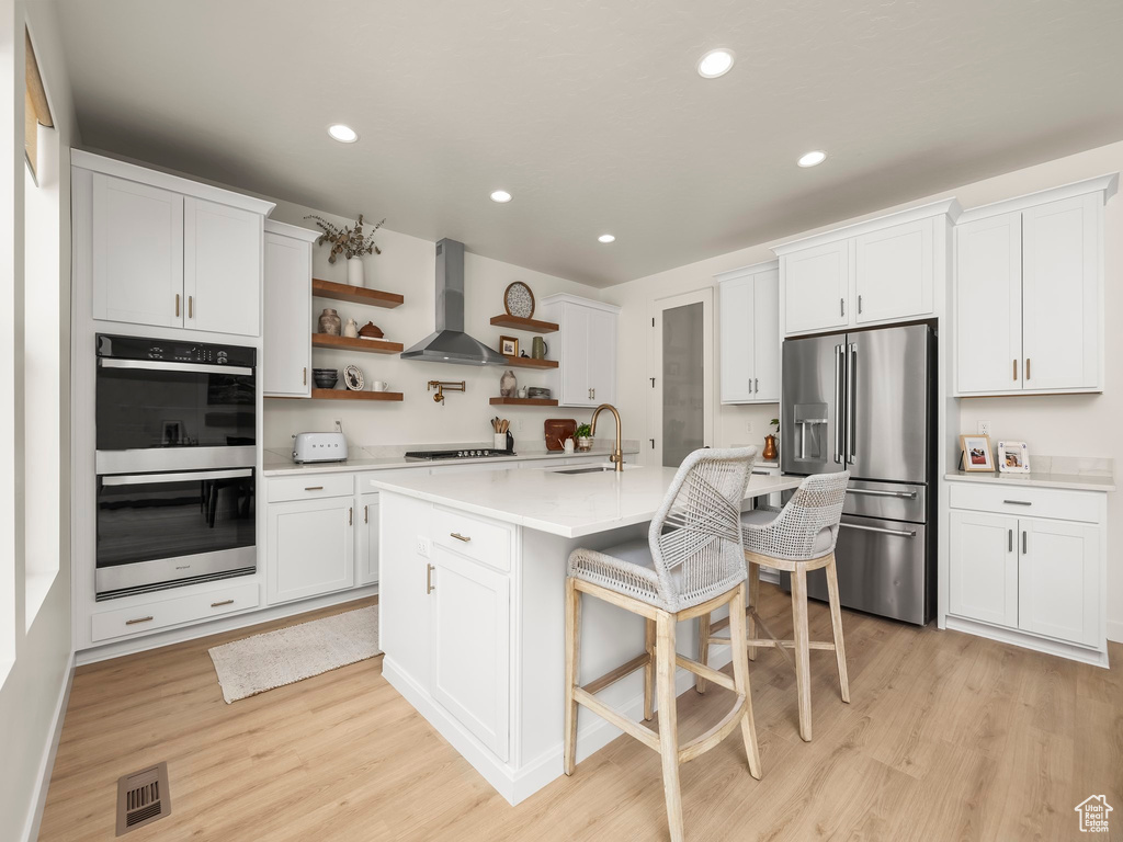 Kitchen featuring appliances with stainless steel finishes, wall chimney range hood, open shelves, light countertops, and light wood-style floors