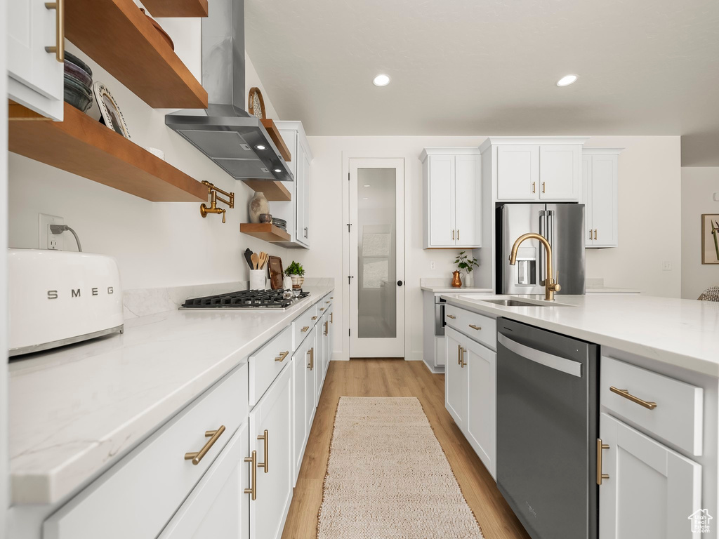Kitchen with appliances with stainless steel finishes, exhaust hood, light wood-type flooring, white cabinetry, and light countertops