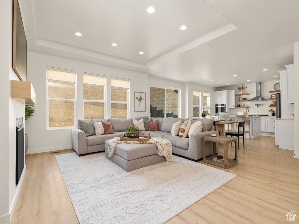 Living area with a tray ceiling, light wood-style flooring, recessed lighting, and a fireplace