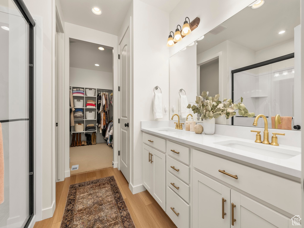 Bathroom with a shower stall, double vanity, wood finished floors, a spacious closet, and recessed lighting