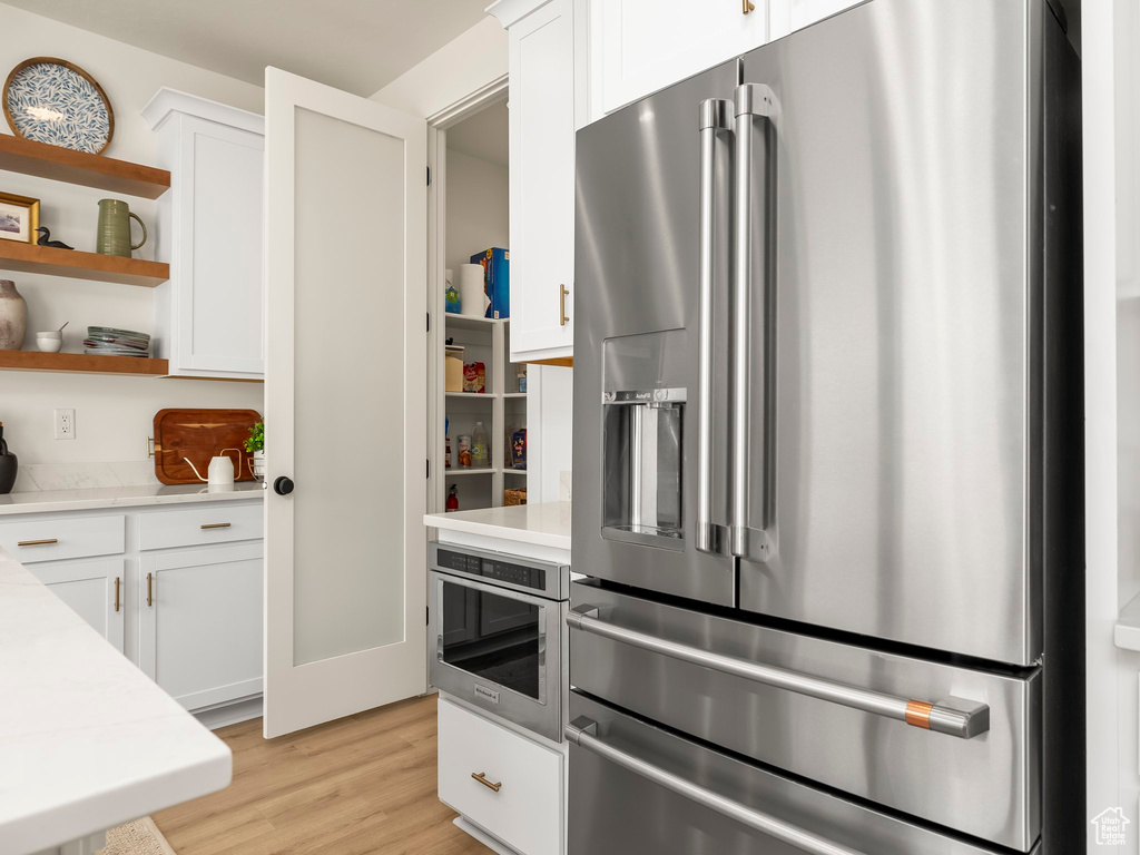 Kitchen featuring stainless steel refrigerator with ice dispenser, open shelves, light countertops, and white cabinets