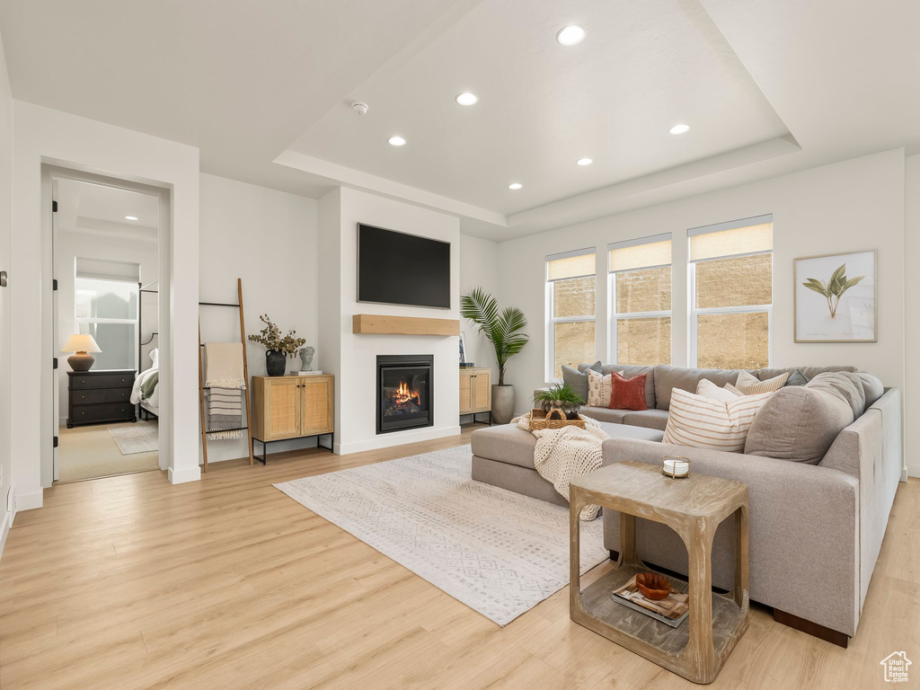 Living room with a tray ceiling, light wood-style floors, recessed lighting, and a glass covered fireplace