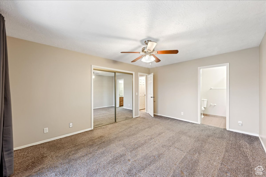 Unfurnished bedroom with carpet floors, ensuite bathroom, a ceiling fan, a textured ceiling, and two closets
