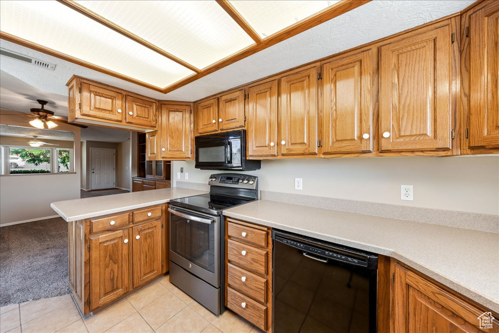 Kitchen with black appliances, a peninsula, brown cabinetry, and light countertops