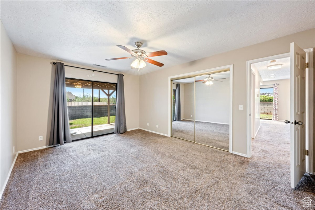 Unfurnished bedroom with multiple windows, a textured ceiling, carpet flooring, access to outside, and a ceiling fan
