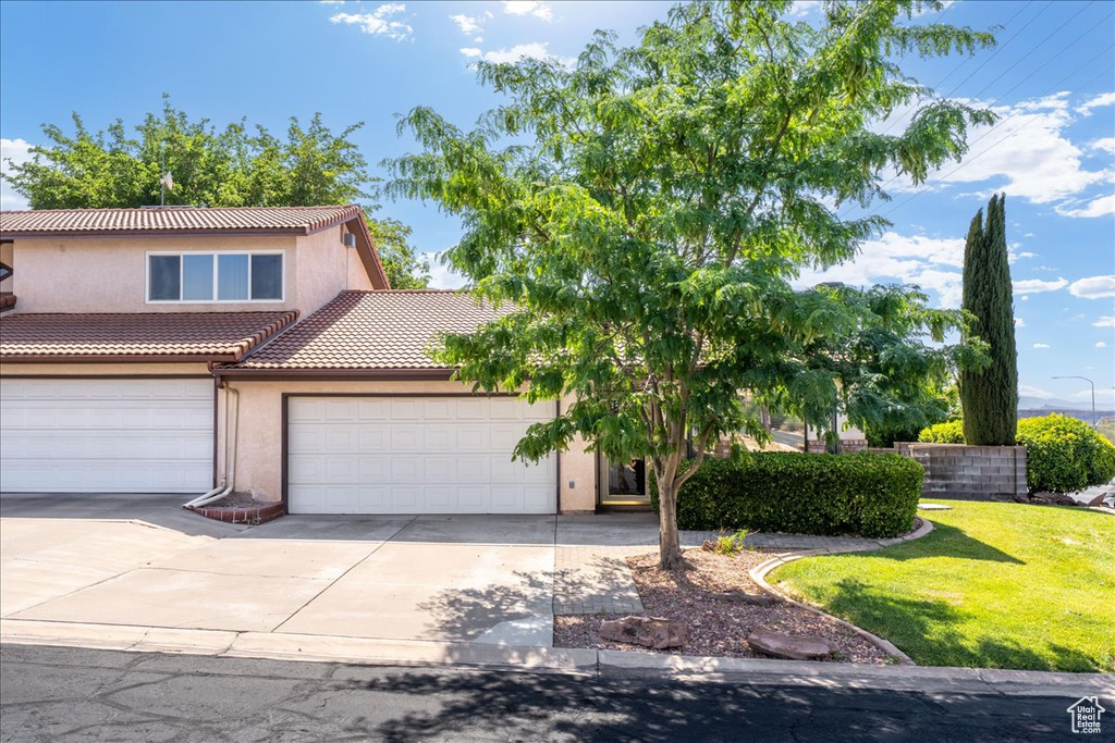 View of front of property featuring an attached garage, stucco siding, concrete driveway, a front lawn, and a tile roof
