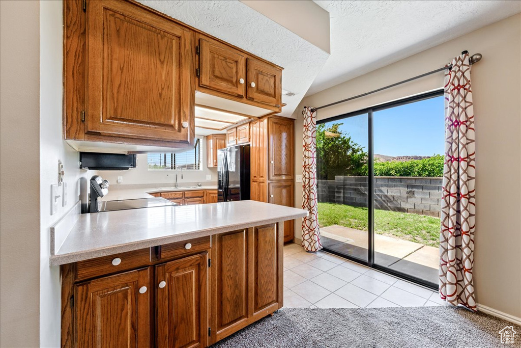 Kitchen featuring black fridge, stove, light countertops, brown cabinets, and a peninsula