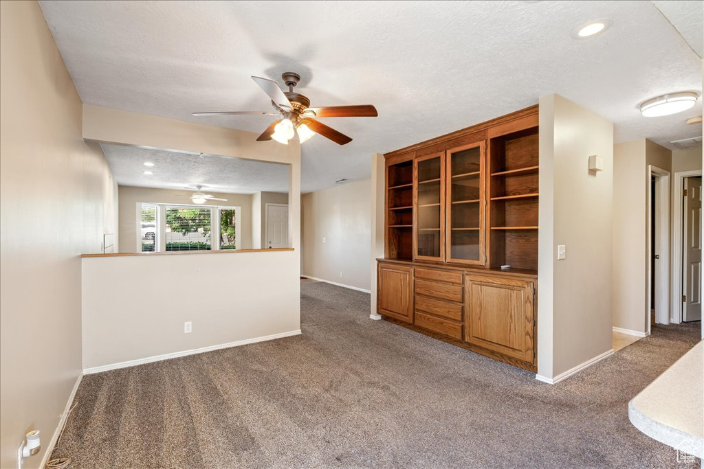 Unfurnished living room featuring carpet flooring, a ceiling fan, and a textured ceiling