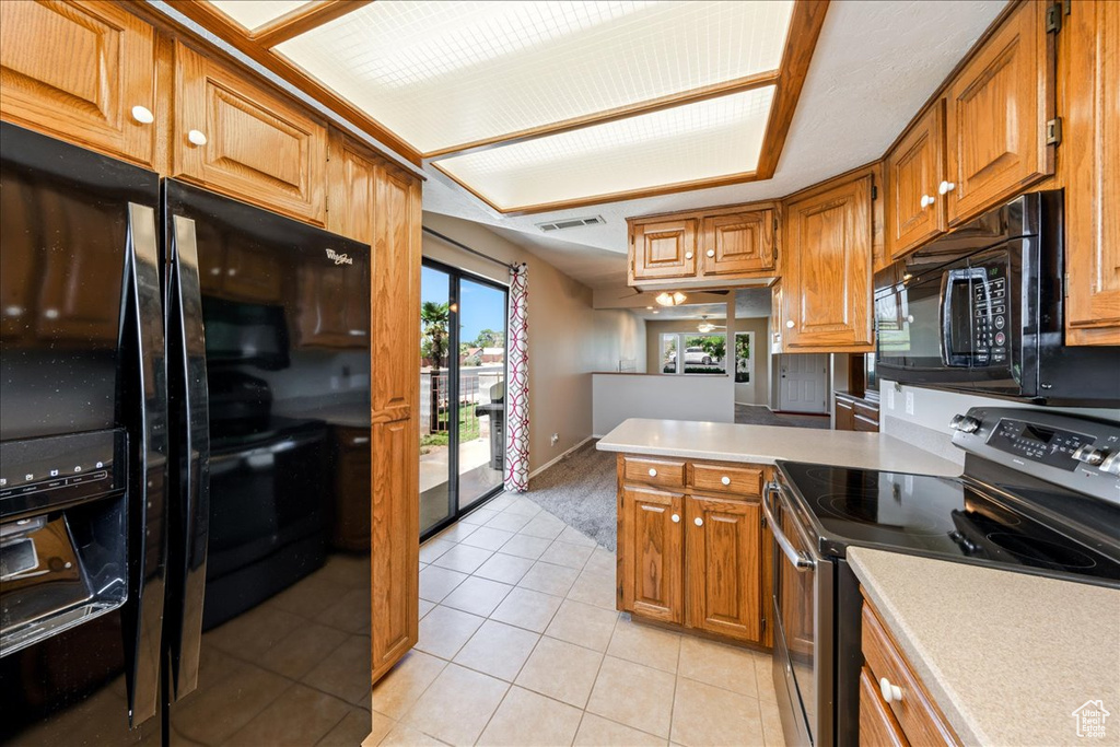 Kitchen featuring black appliances, a peninsula, light tile patterned floors, and brown cabinets