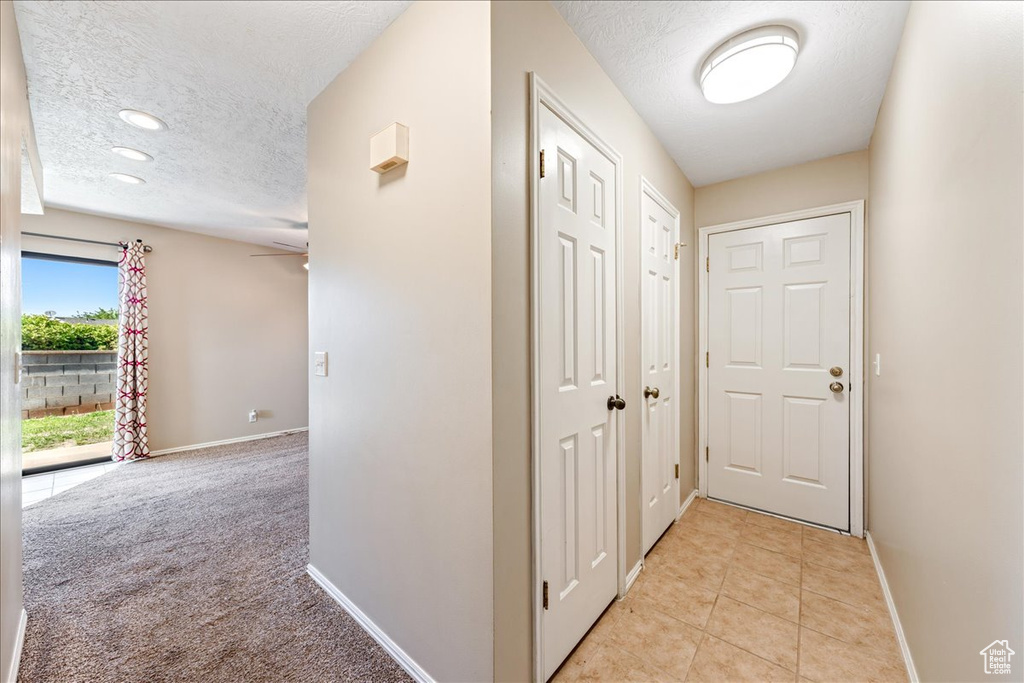 Hallway featuring a textured ceiling, light tile patterned floors, light colored carpet, and recessed lighting