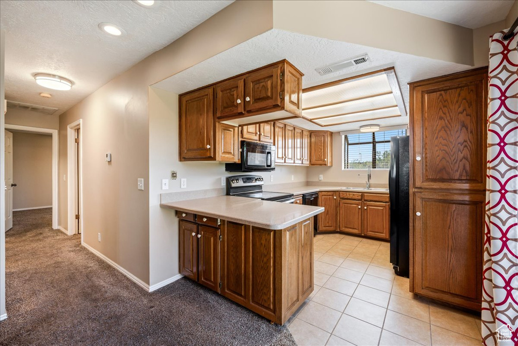 Kitchen featuring black appliances, a peninsula, light countertops, a textured ceiling, and brown cabinets