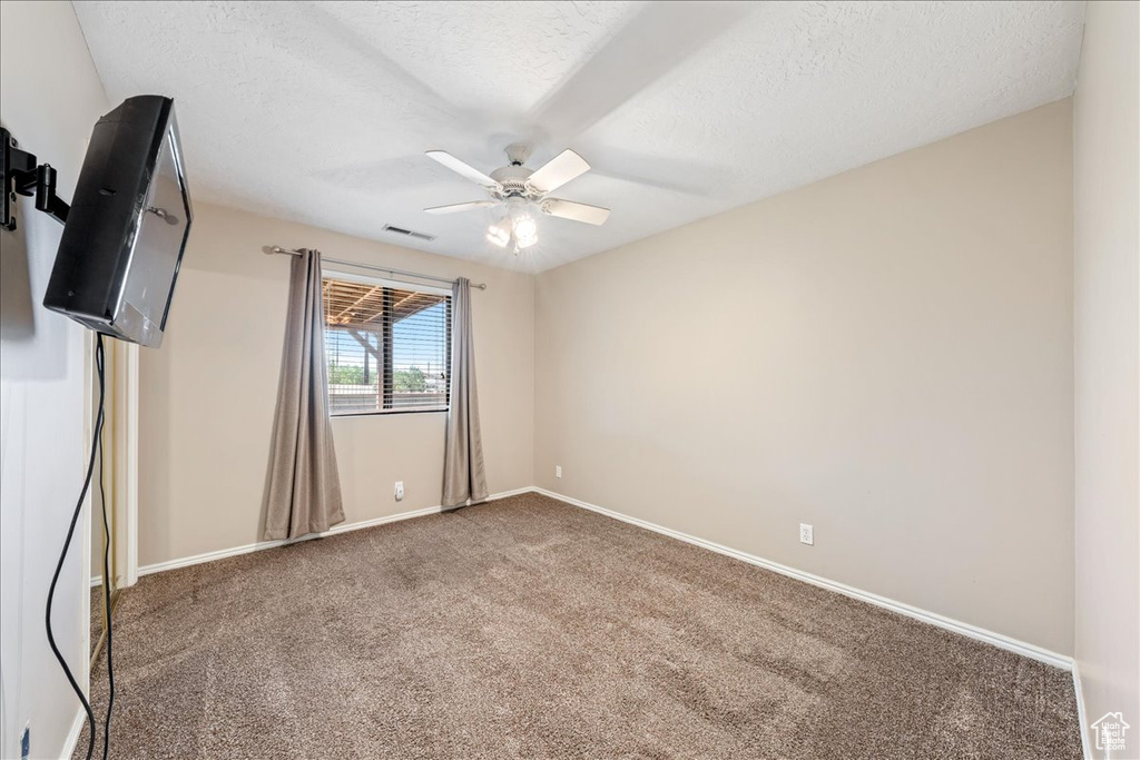 Carpeted empty room featuring ceiling fan and a textured ceiling
