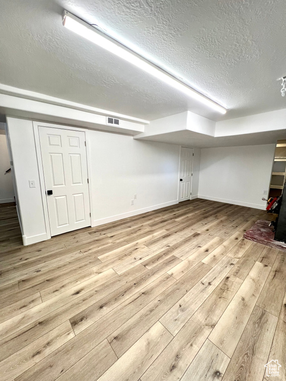 Finished below grade area with a textured ceiling and light wood-style floors
