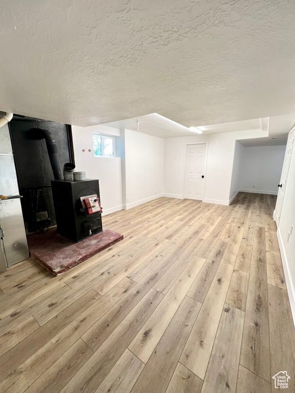 Basement with a wood stove, light wood-style floors, and a textured ceiling