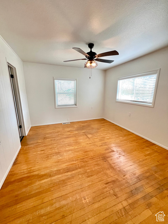 Unfurnished room featuring light wood finished floors, healthy amount of natural light, a ceiling fan, and a textured ceiling