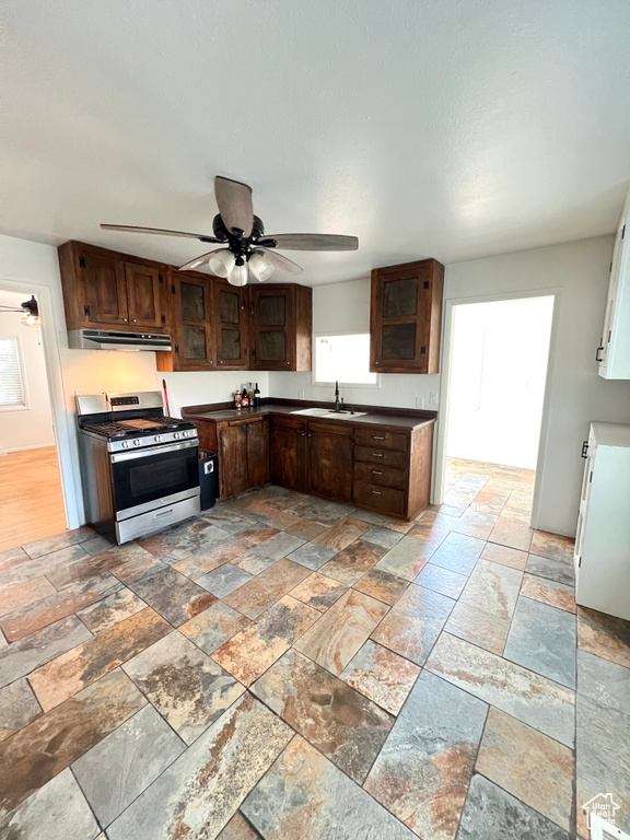 Kitchen featuring stainless steel gas stove, under cabinet range hood, a ceiling fan, and stone tile flooring