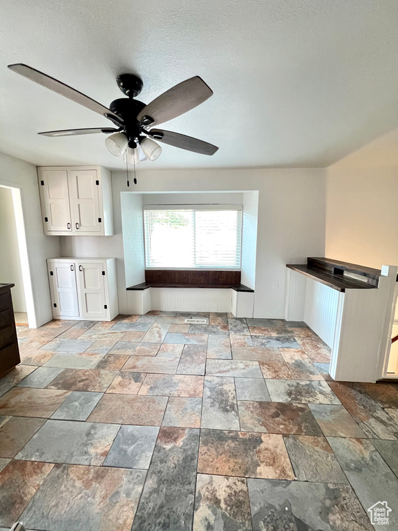 Kitchen with stone tile floors, a ceiling fan, and white cabinetry