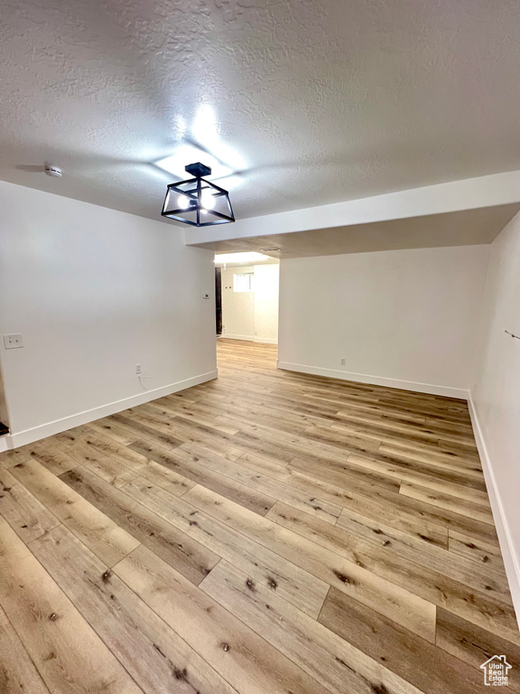 Unfurnished room with light wood-style flooring, a textured ceiling, and a smoke detector