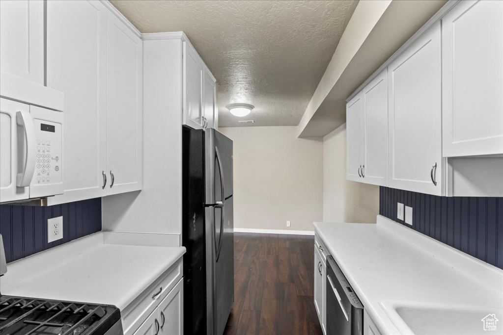 Kitchen featuring appliances with stainless steel finishes, a textured ceiling, white cabinets, light countertops, and dark wood-type flooring
