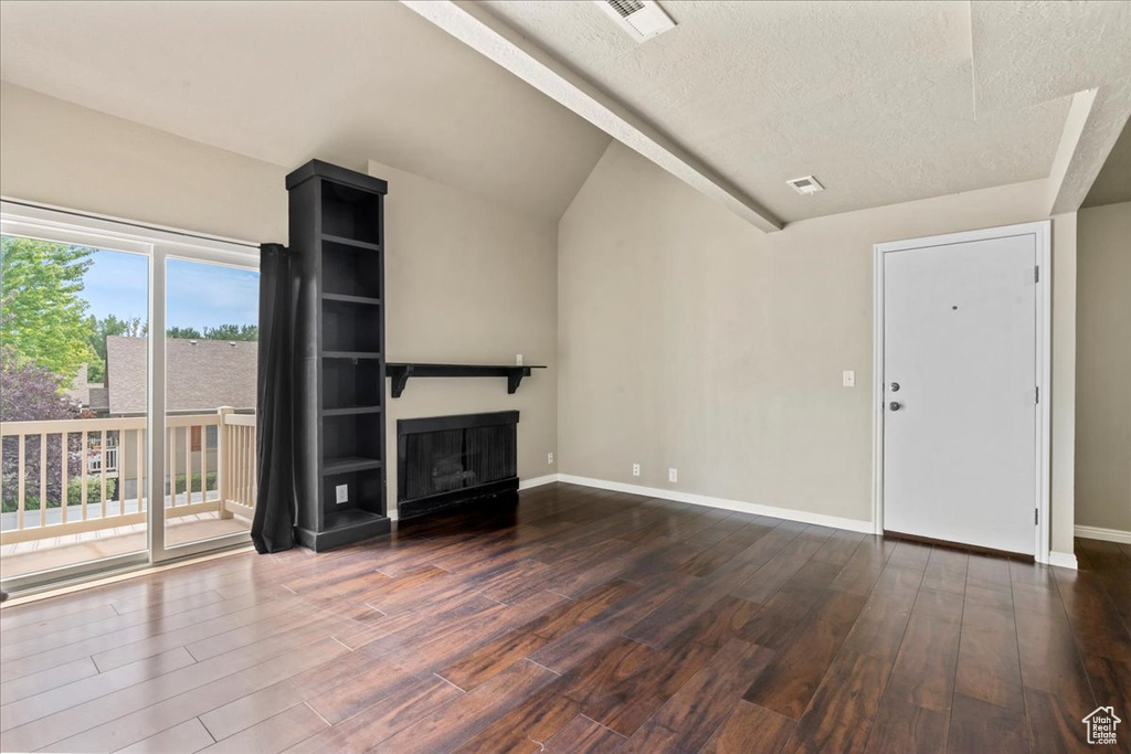 Unfurnished living room with wood finished floors, a textured ceiling, vaulted ceiling, and a glass covered fireplace