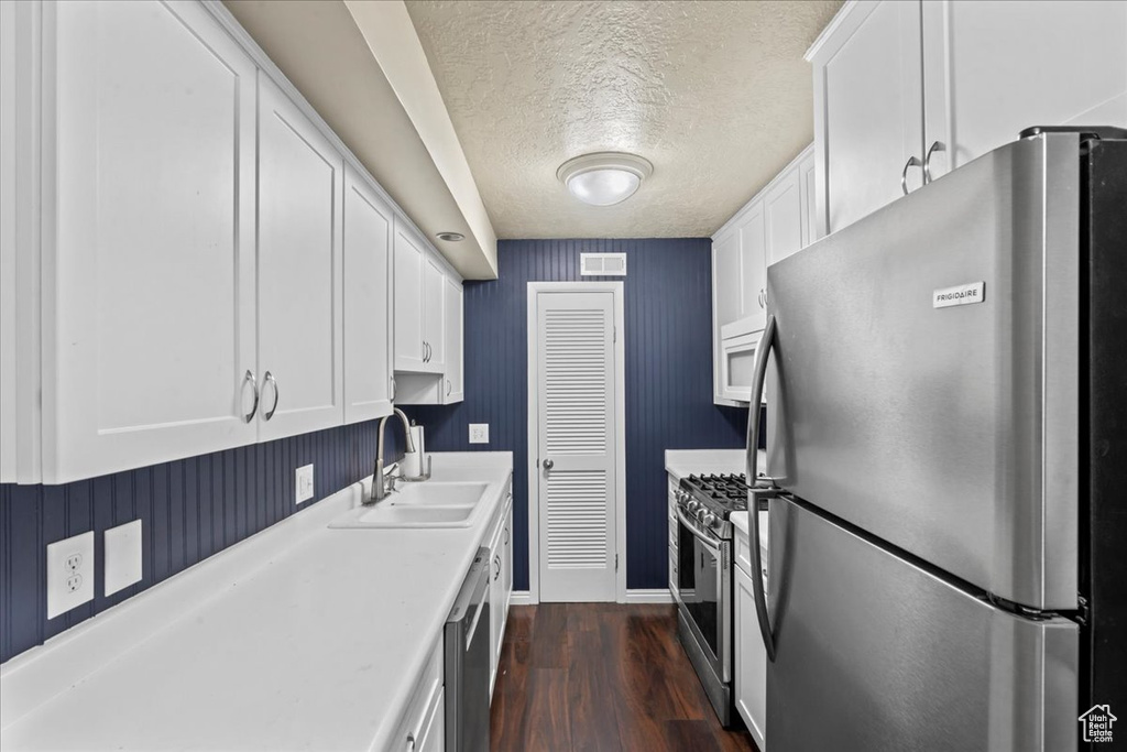 Kitchen featuring stainless steel appliances, a textured ceiling, white cabinetry, light countertops, and dark wood-type flooring