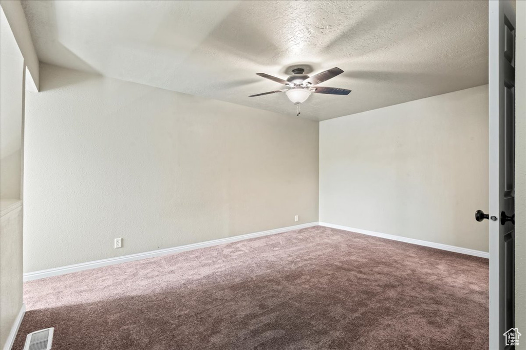 Carpeted empty room featuring ceiling fan and a textured ceiling