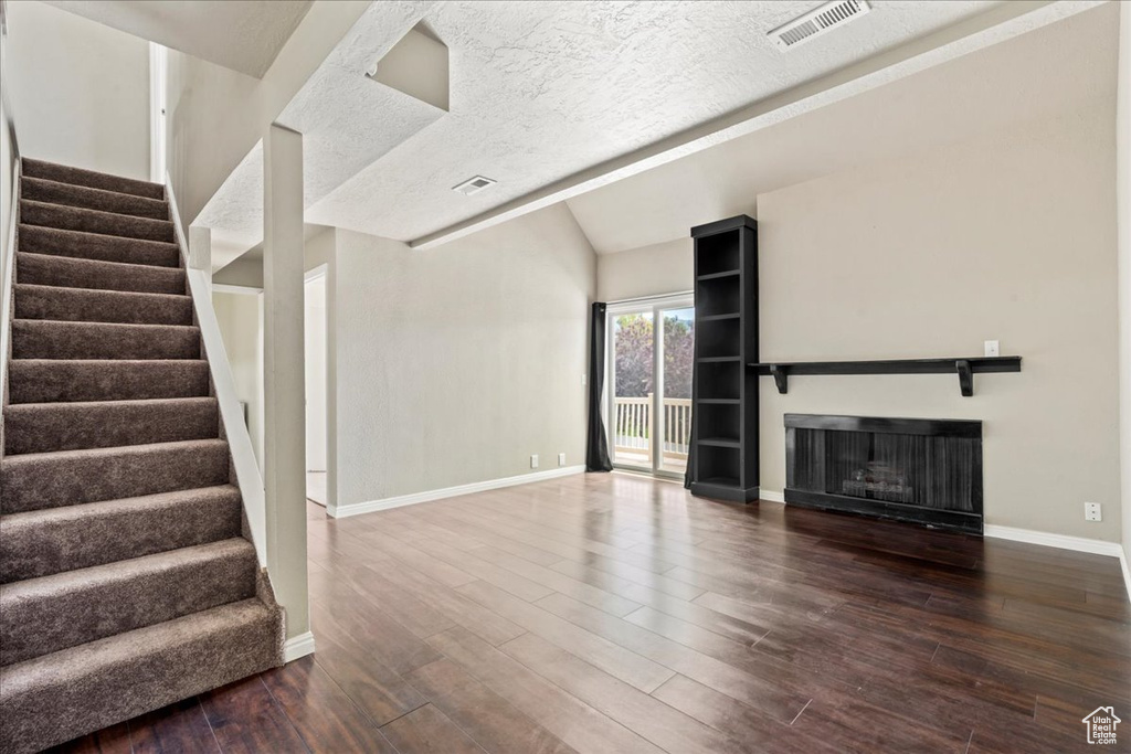 Unfurnished living room featuring wood finished floors, stairway, vaulted ceiling, and a fireplace
