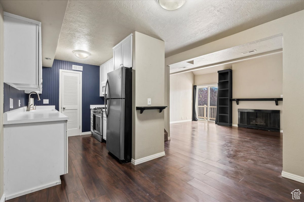 Kitchen featuring appliances with stainless steel finishes, a textured ceiling, white cabinetry, dark wood-type flooring, and light countertops