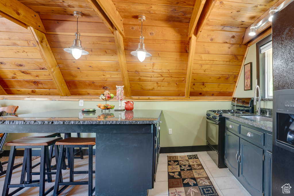Kitchen featuring black gas range oven, wood ceiling, light tile patterned floors, a breakfast bar area, and decorative light fixtures