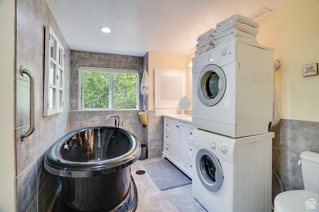 Full bath with tile walls, stacked washer / drying machine, a freestanding tub, and a textured ceiling