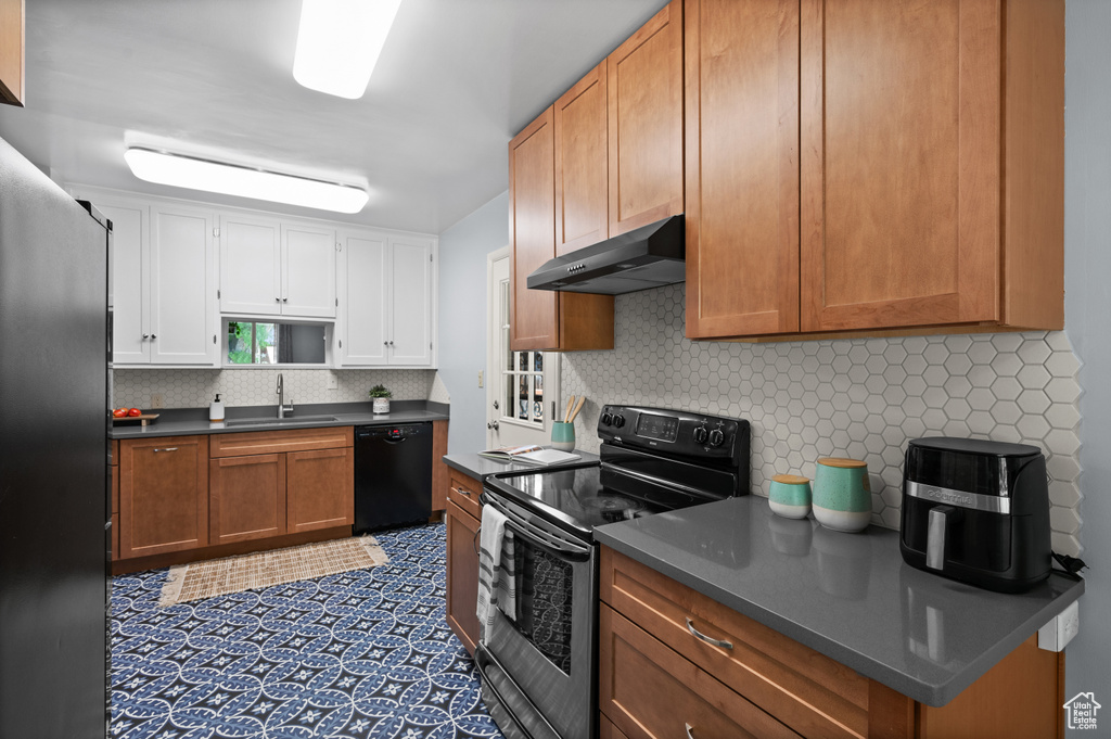 Kitchen with stainless steel appliances, under cabinet range hood, dark countertops, decorative backsplash, and white cabinetry