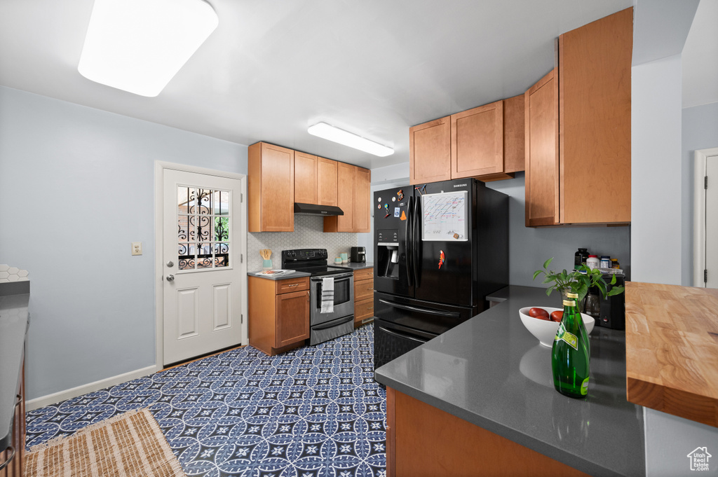 Kitchen with stainless steel range with electric cooktop, black fridge, and under cabinet range hood